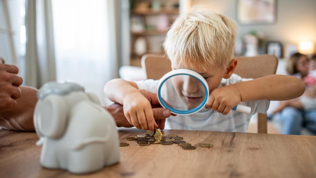 Niño examinando unas monedas con lupa.