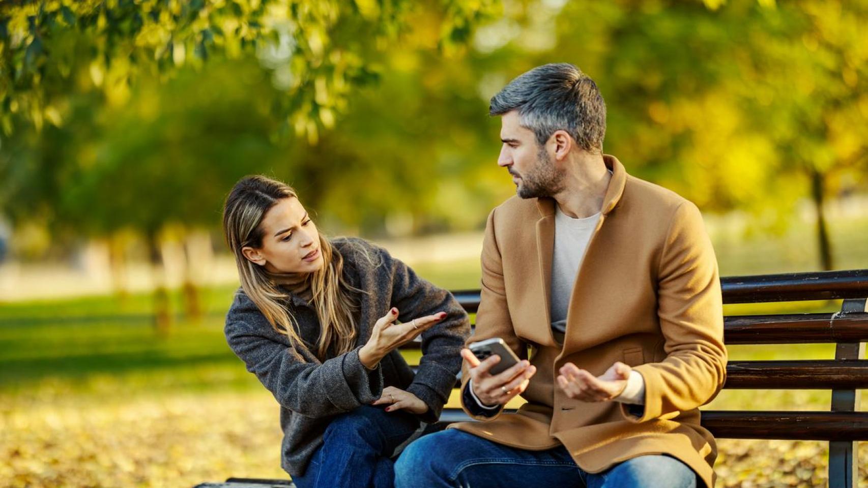 Una pareja discutiendo por el móvil en un parque.