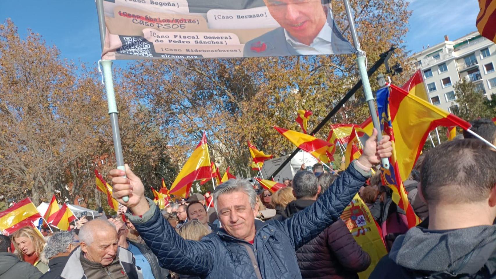 Un asistente a la concentración en el Templo de Debod (Madrid) sostiene un cartel con el rostro de Sánchez y los casos judiciales que envuelven a su círculo.