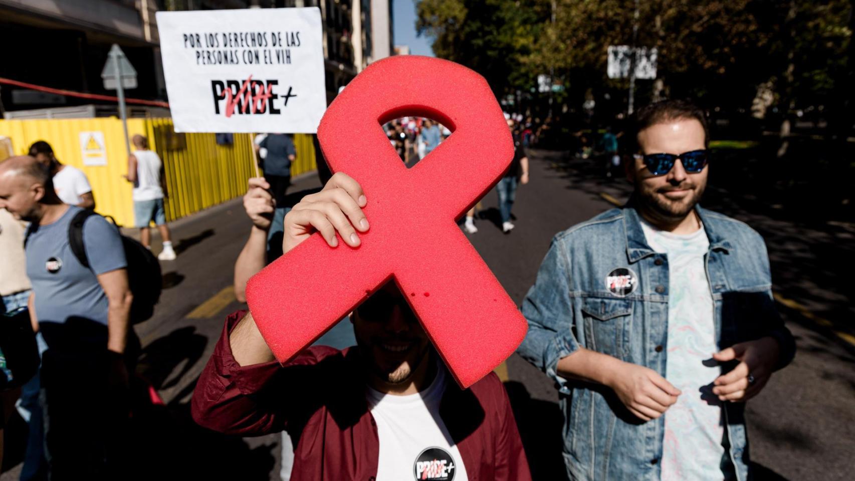 Manifestantes portan un lazo rojo y pancarta con lema 'Por los derechos de las personas con VIH' durante la Cuarta Marcha Positiva organizada por Pride Positivo, a 18 de octubre de 2025, en Madrid (España).