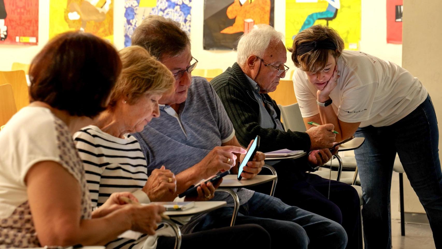 Una voluntaria de la Fundación Cibervoluntarios enseña a un grupo de personas a utilizar un teléfono móvil.