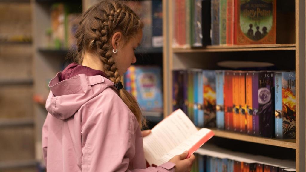 Unha nena le un libro na biblioteca.