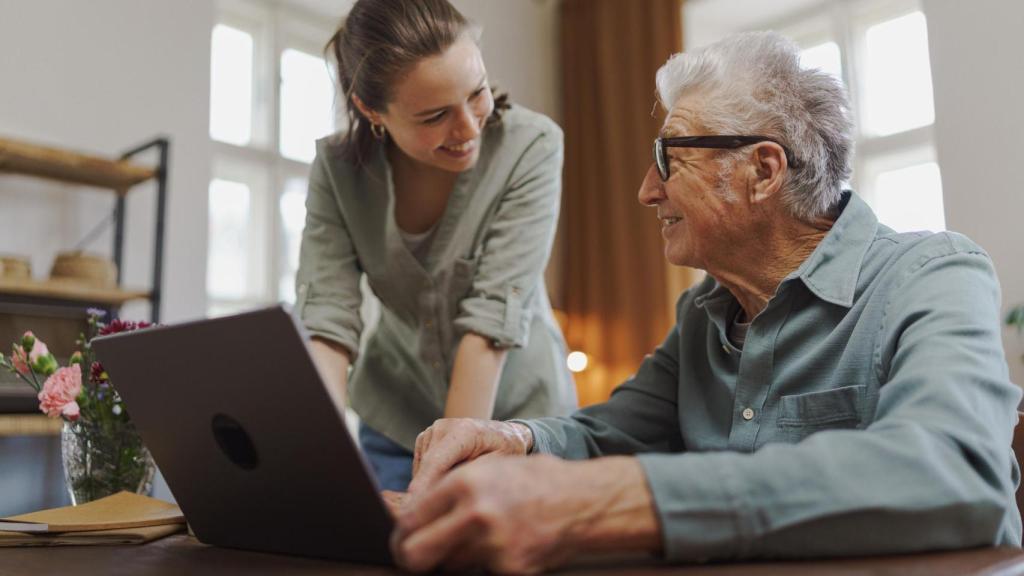 Una persona ayudando a un señor a utilizar el ordenador.