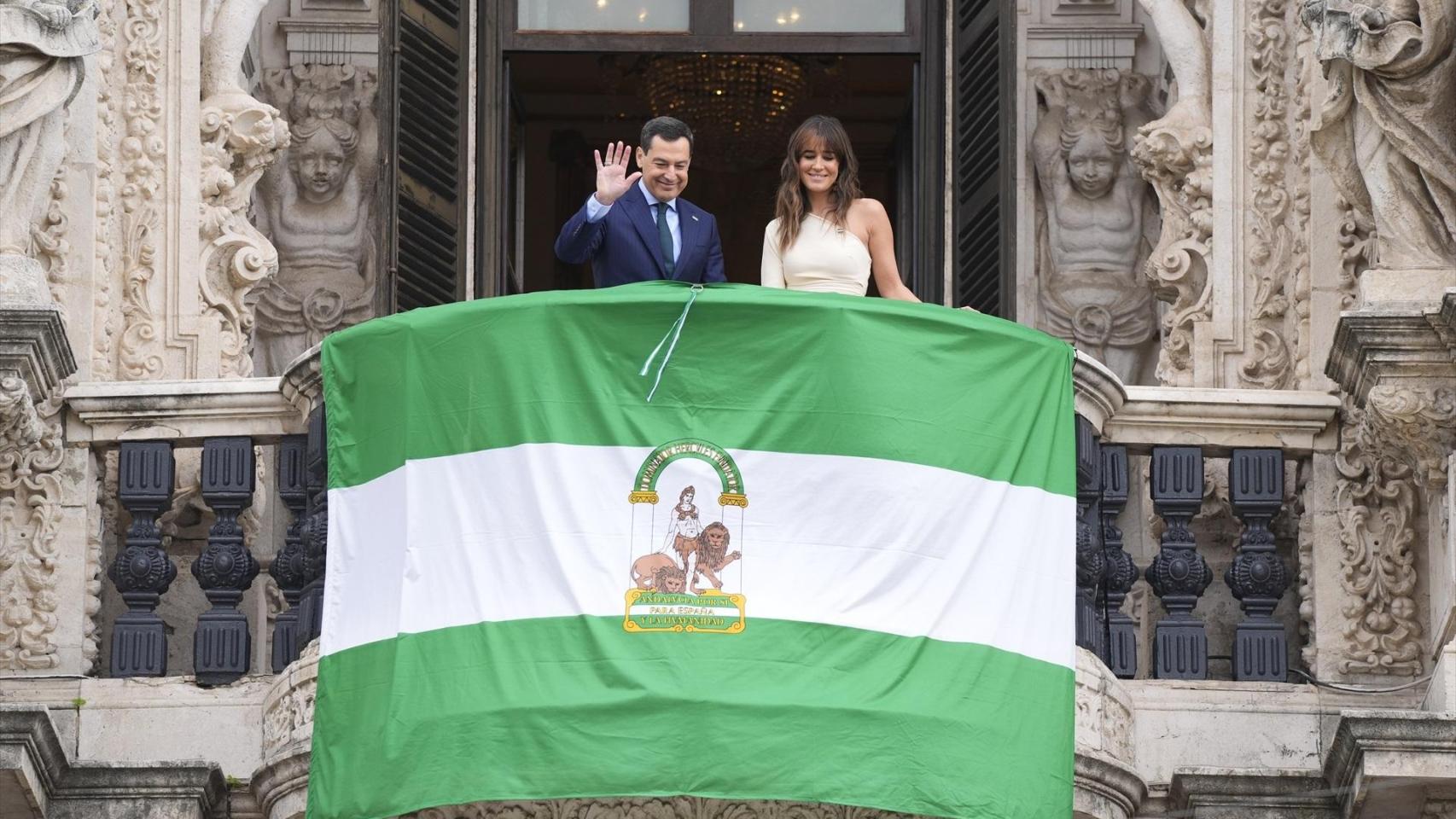 Juanma Moreno y la periodista Isabel Jiménez despliegan la bandera de Andalucía en San Telmo.