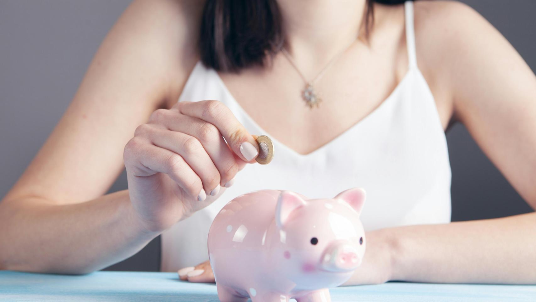 Una ahorradora metiendo una moneda en una hucha.