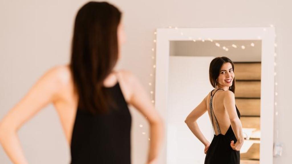 Mujer vestida de fiesta mirándose en el espejo.