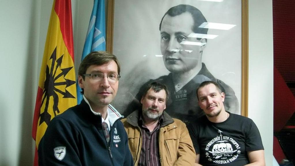 Varios miembros del Movimiento Imperial Ruso, durante una visita a España, posando junto a la bandera falangista y una imagen de José Antonio.