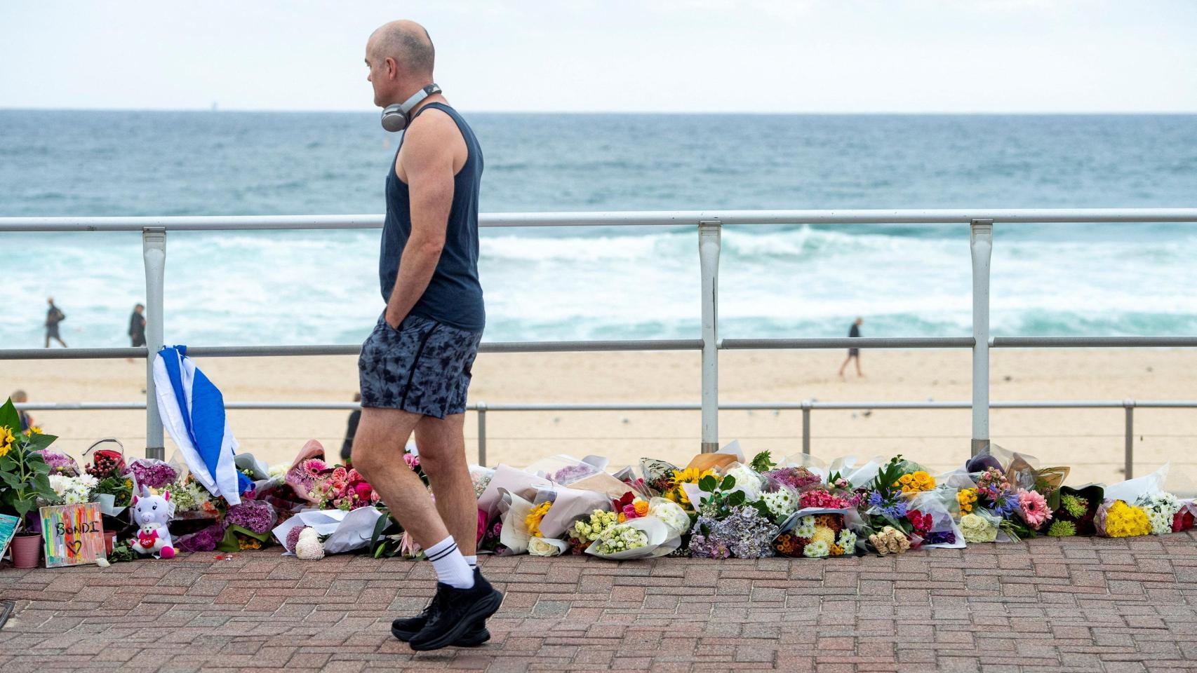 Un hombre camina por la playa de Bondi delante de uno de los memoriales improvisados a las víctimas.
