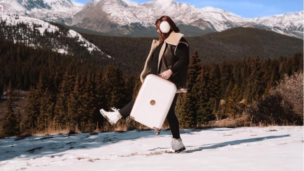 Una chica con una maleta Delsey Paris en la nieve.