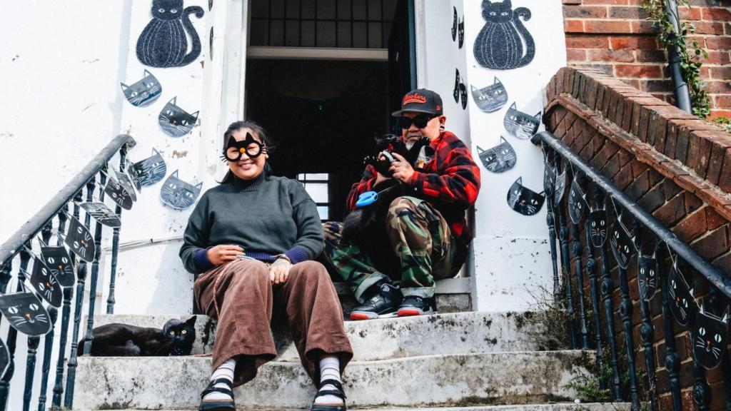 Un chico y una chica sentados con un gato negro en brazos.