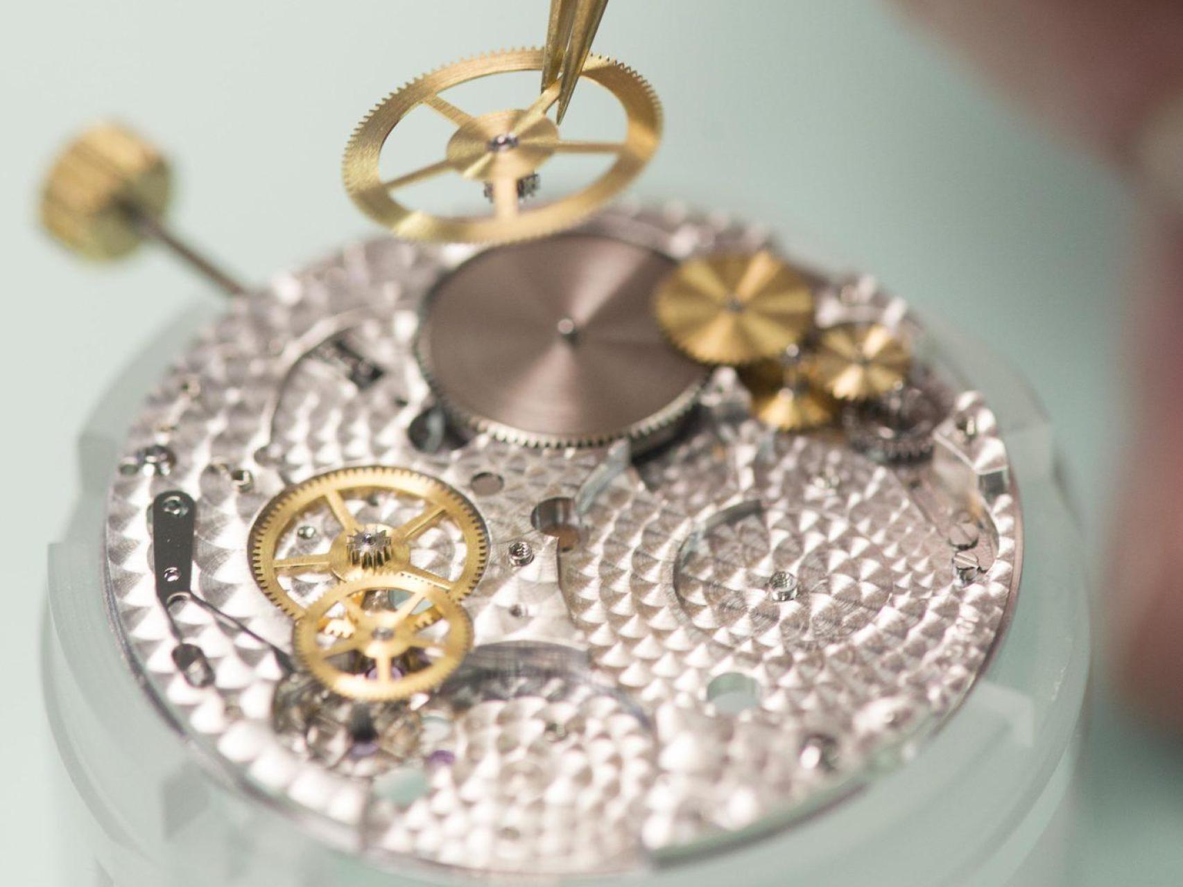 El interior de un reloj mecánico mientras que un relojero trabaja sobre el movimiento de la pieza.