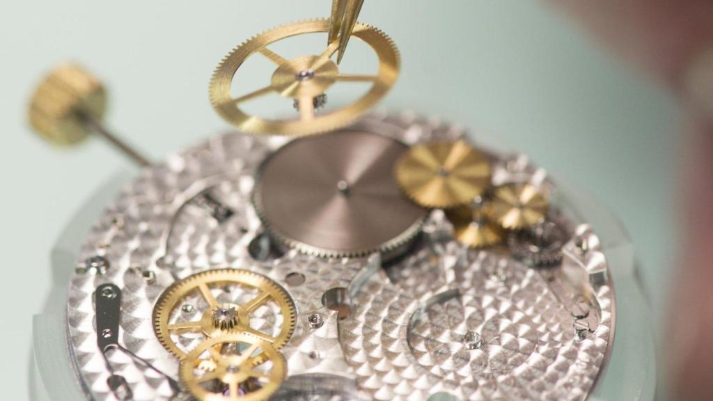 El interior de un reloj mecánico mientras que un relojero trabaja sobre el movimiento de la pieza.