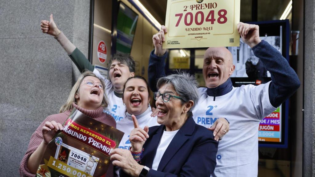 Varias personas celebran a las puertas de la administración de loterías del número 10 de la calle Barquillo, en Madrid, donde se ha vendido íntegramente el 70.048, el segundo premio.