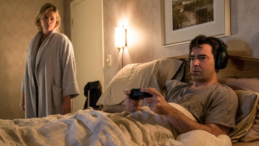 Charlize Theron en otro 'frame' de 'Tully' (2018), físicamente agotada, mientras observa cómo su pareja se divierte jugando desde la cama.