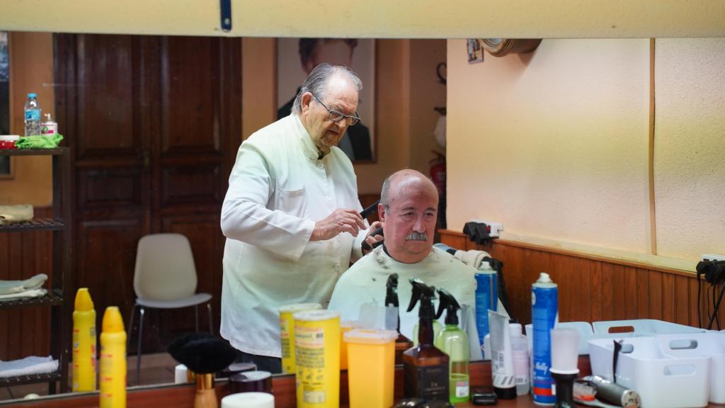 Enrique Colomer (88 años) corta el pelo a uno de sus clientes.