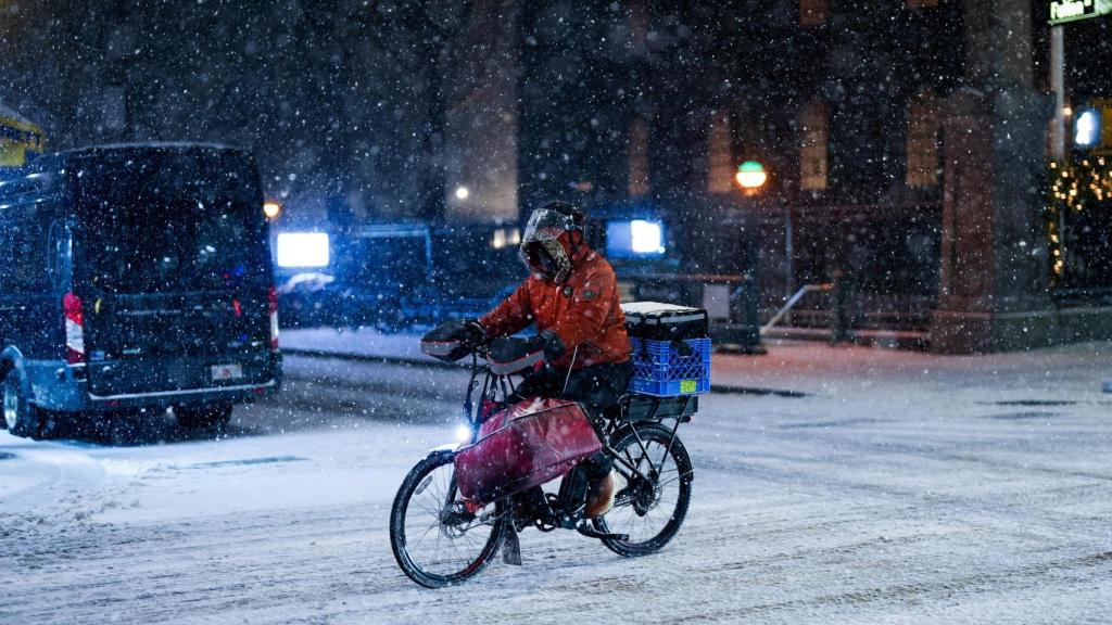 Un repartidor en bicicleta navega mientras cae nieve durante una tormenta invernal en la ciudad de Nueva York