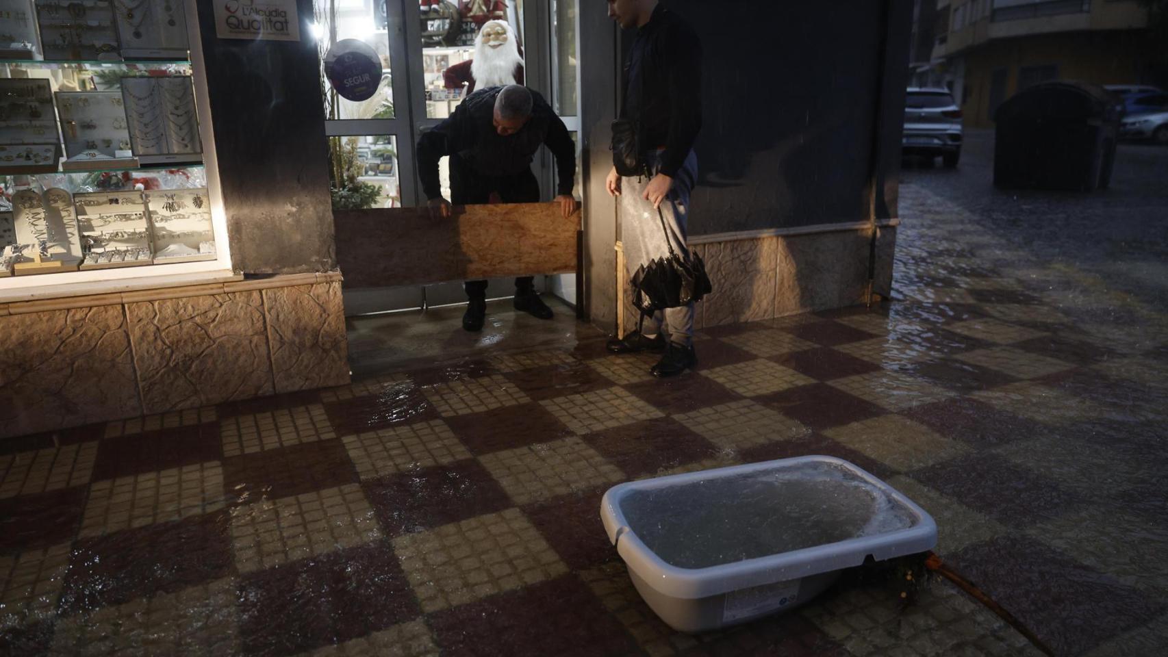 Un hombre coloca una barrera en la puerta de su comercio para evitar la entrada del agua durante la tormenta registrada en la localidad de l'Alcúdia (Valencia).