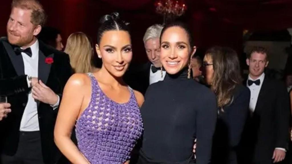 Meghan posando con Kim Kardashian. Harry aparece detrás.