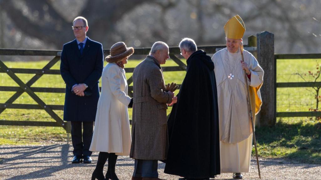El rey Carlos III y Camilla saludan al párroco Paul Williams al llegar a la iglesia de Santa María Magdalena en Sandringham.