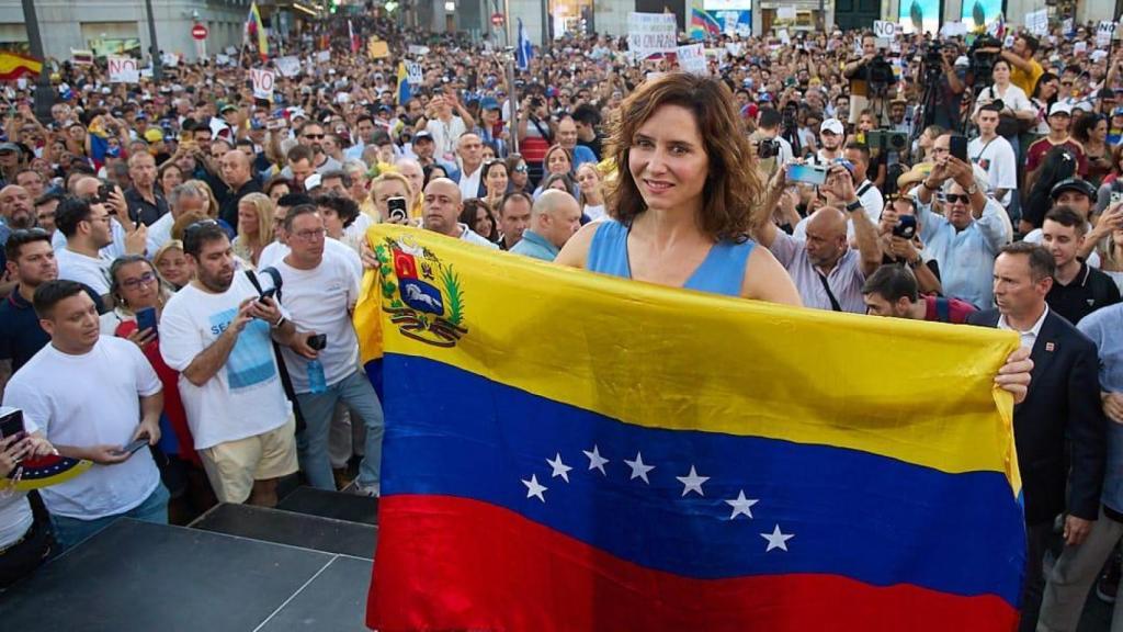 Isabel Díaz Ayuso en la Puerta del Sol luce una bandera de Venezuela durante una manifestación.