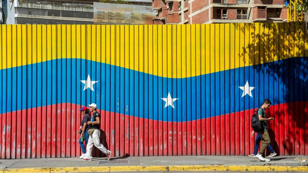 Ciudadanos caminan delante de una bandera venezolana en Caracas