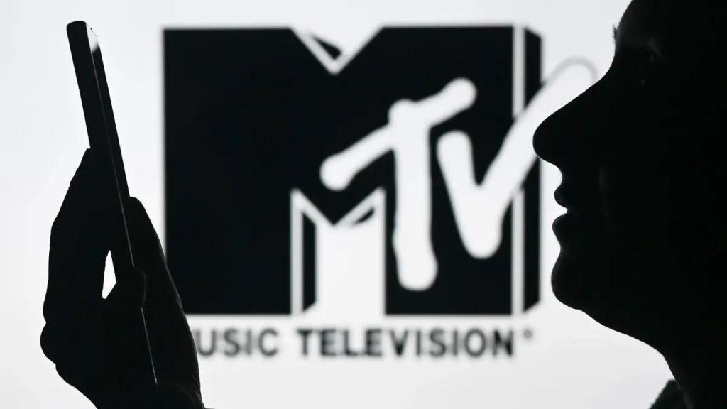 Una mujer mirando su teléfono móvil delante del logo de la MTV.