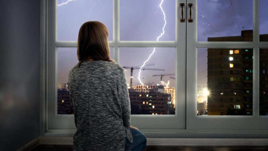 Una mujer viendo la tormenta desde casa.