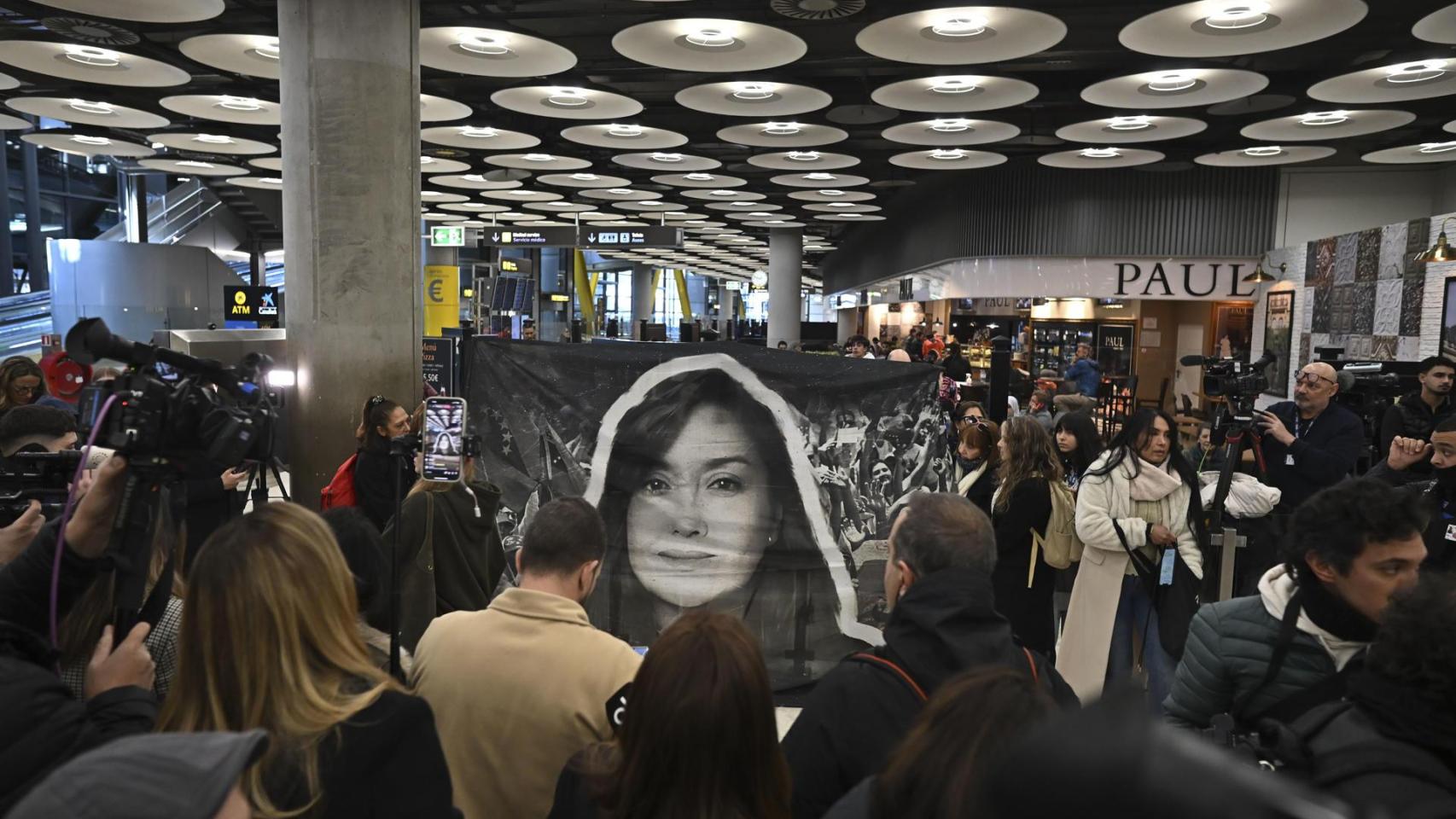 Un grupo de personas sostiene una pancarta con la foto de Rocío San Miguel en el aeropuerto madrileño de Barajas.