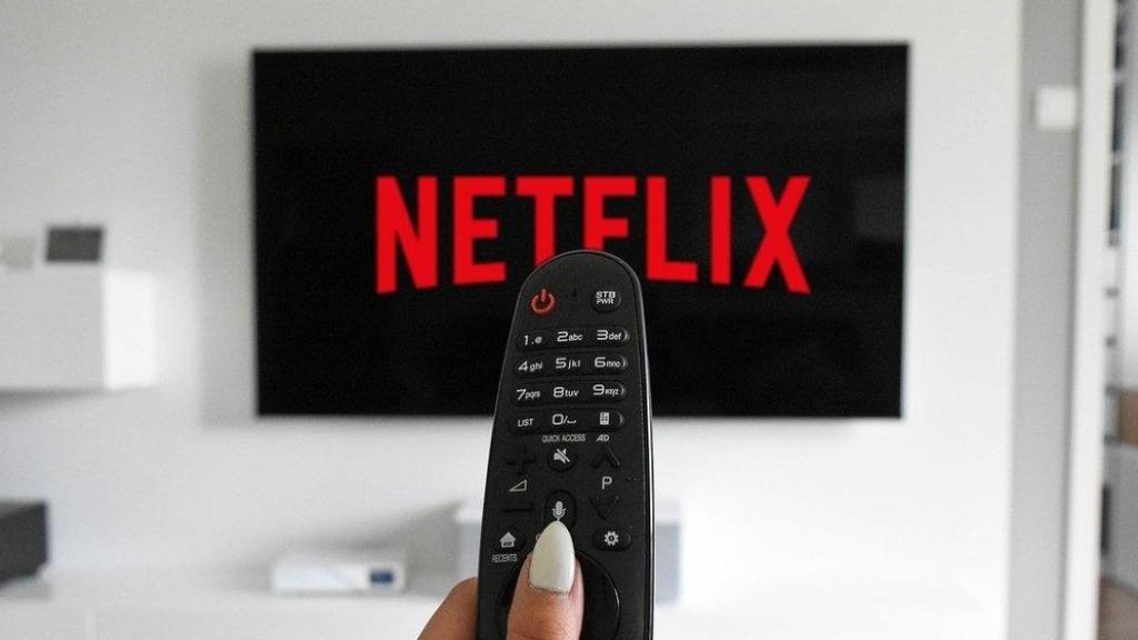 Logo de Netflix en una televisión, con una mujer utilizando un mando a distancia.