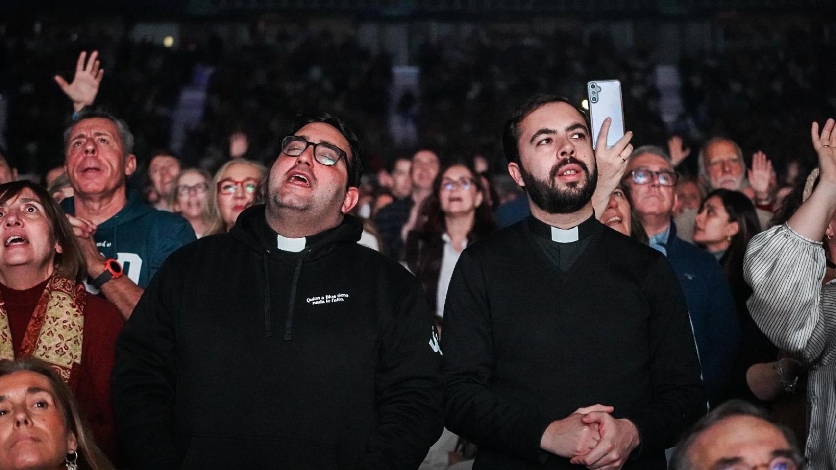 Dos curas junto al público, disfrutando del concierto inicial de 'Llamados: Unidos hacia el 2033'.