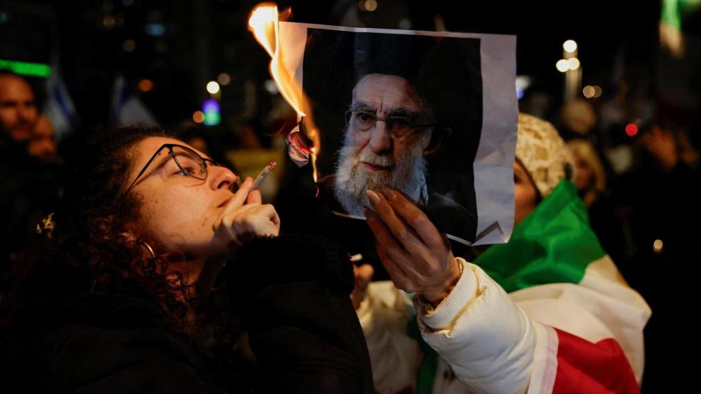 Una mujer enciende un cigarrillo con el fuego de una foto en llamas del líder supremo de Irán, el ayatolá Alí Jameneí, en Holon, Israel.