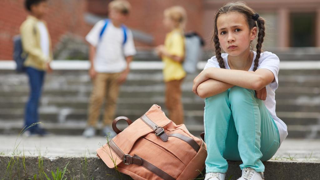 Una niña sentada frente a su escuela.
