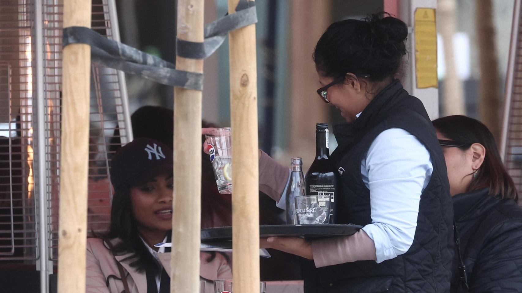 Una camarera atendiendo clientes en una terraza.