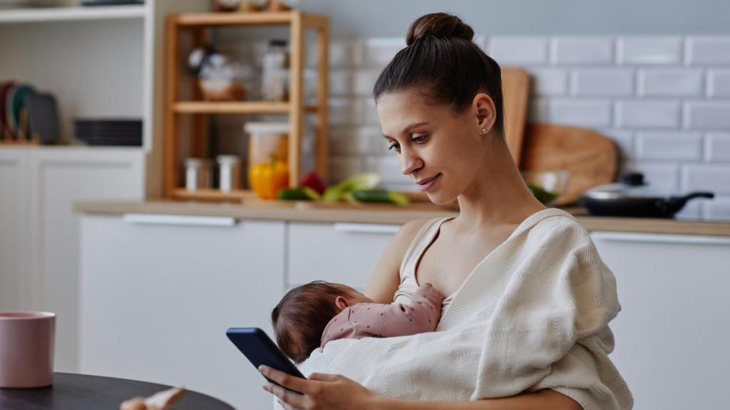 Imagen de archivo de una mujer usando el móvil mientras sostiene a su hijo.