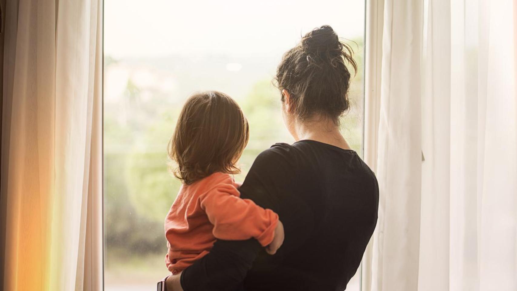 Una madre con su bebé mirando por la ventana.