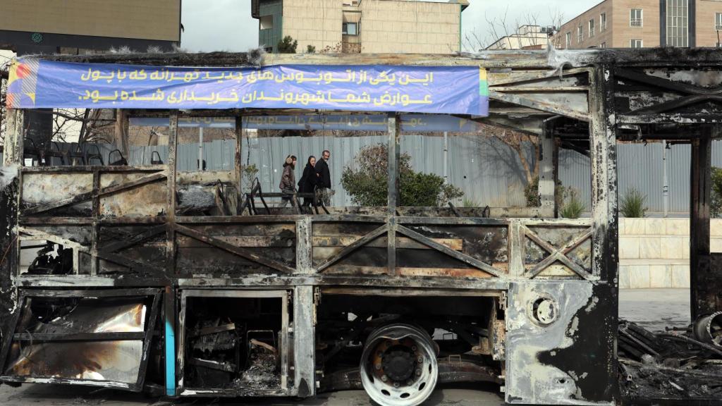 Iraníes caminan junto a los restos de un autobús público incendiado en Teherán (Irán)
