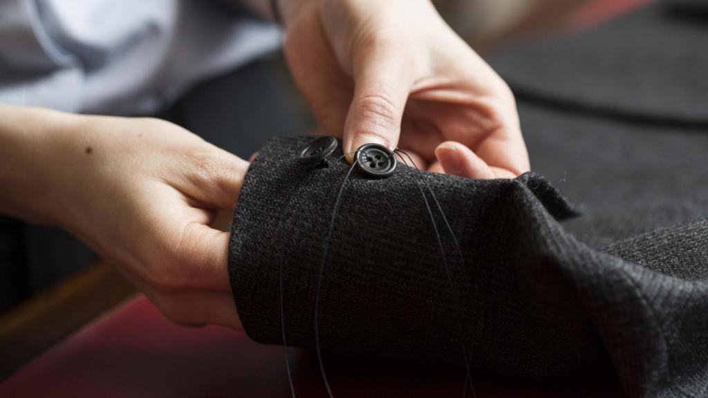 Kathryn Sargent cosiendo el botón de la manga de un traje de chaqueta.