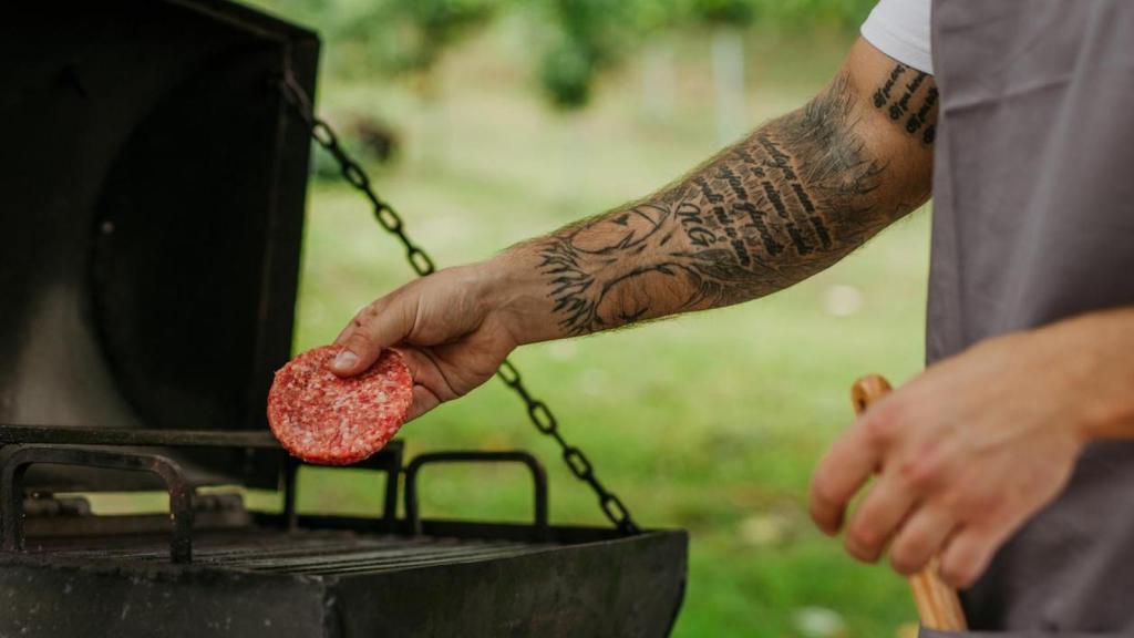 Un hombre cocina una hamburguesa a la parrilla.