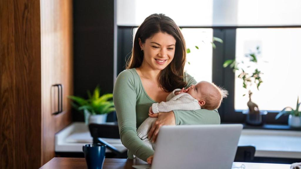 Una madre trabajando en remoto con su hijo en brazos.