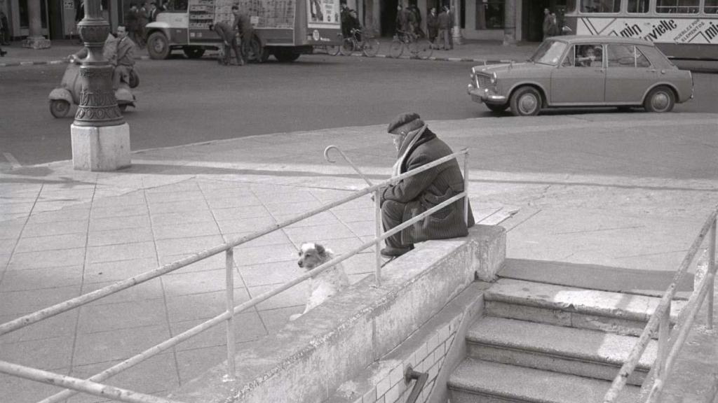 Un anciano acompañado de un perro sentado en la entrada del aparcamiento de la Plaza Mayor, en la década de los 70