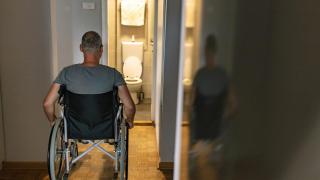 Un persona en silla de ruedas frente a un baño que no está adaptado.