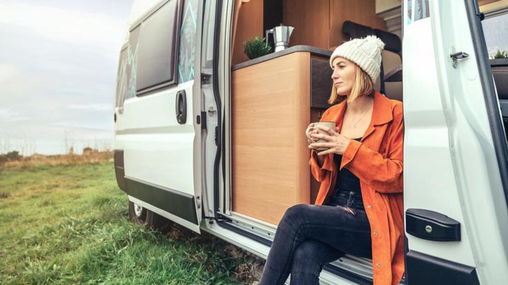 Mujer sentada en su furgoneta camper tomando café.