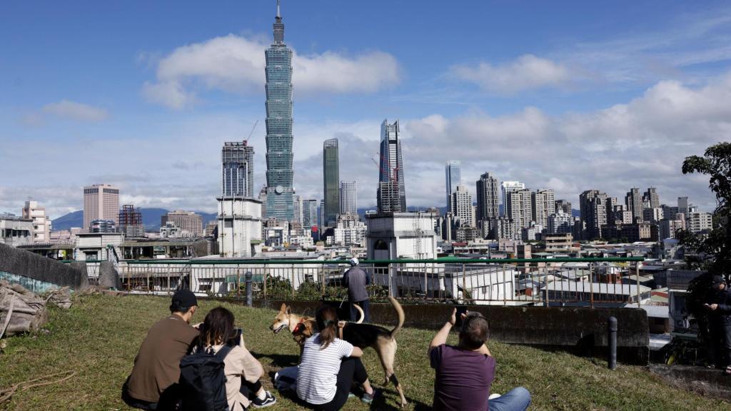 Varias personas observan desde la lejanía cómo Alex Honnold asciende el rascacielos taiwanés Taipei 101.