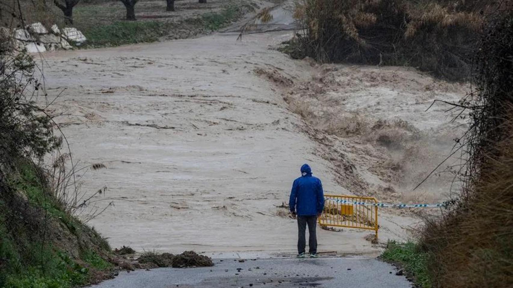 Un hombre observa junto una carretera inundada.