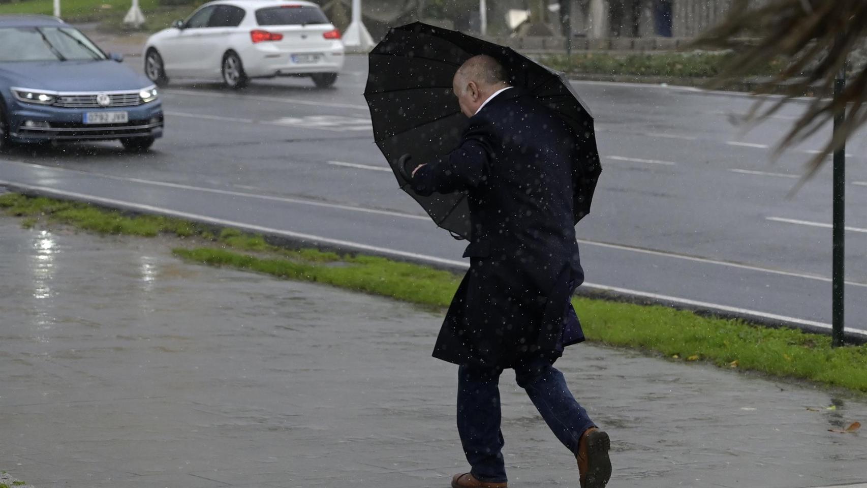 Un hombre con paraguas trata de refugiarse del viento y de la lluvia,en A Coruña.