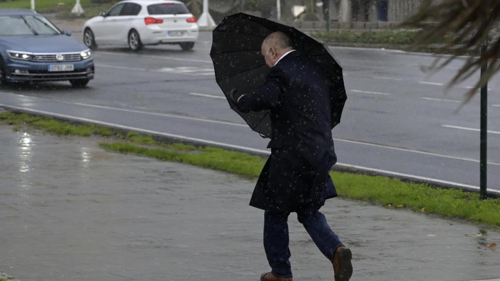 Un hombre con paraguas trata de refugiarse del viento y de la lluvia,en A Coruña.