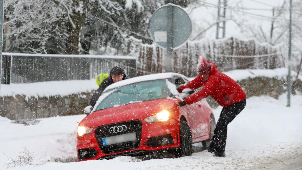Dos personas intentan sacar un vehículo atrapado en la nieve en Madrid.