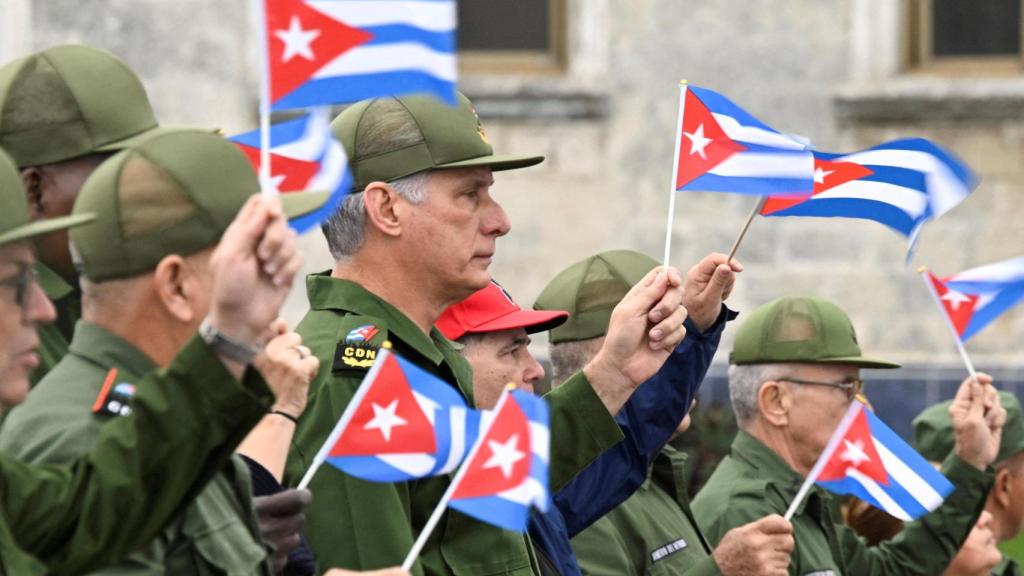 El presidente cubano Miguel Díaz‑Canel ondea una bandera cubana junto con otras personas durante una marcha frente a la Embajada de EEUU.