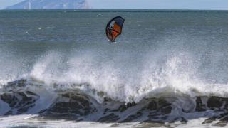 Un surfista aprovecha el fuerte viento para disfrutar de su afición con la Serra Gelada al fondo. EFE/Pep Morell