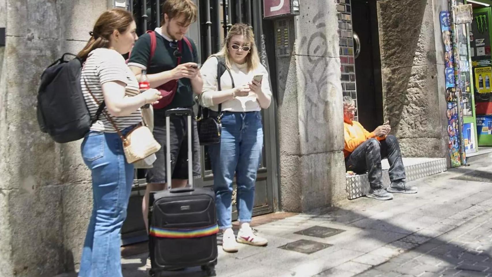 Unos jóvenes esperan frente a un piso de alquiler turístico.